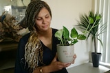 Lousynda, long dark and blonde hair looking down at the pot plant she's holding that says Alo Angel.