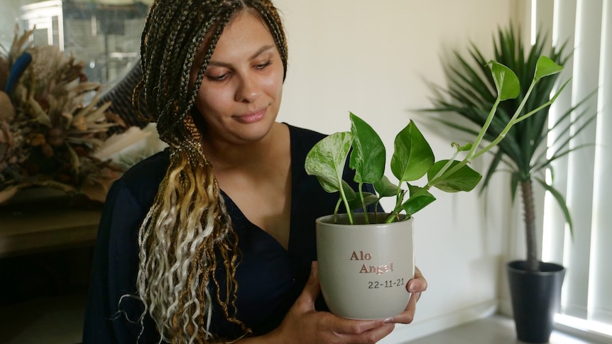 Lousynda, long dark and blonde hair looking down at the pot plant she's holding that says Alo Angel.
