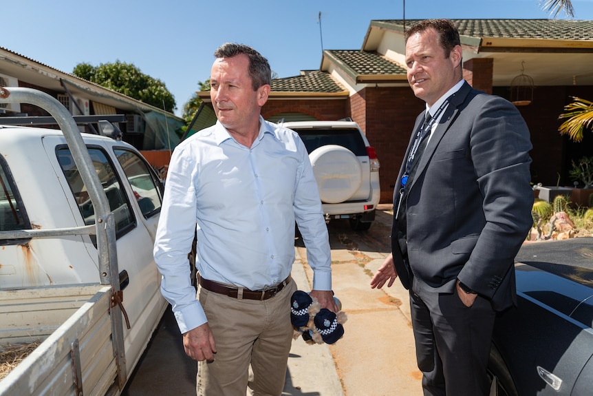 Mark McGowan and Cameron Blaine stand between two cars outside a house, with Mr McGowan holding two teddy bears.