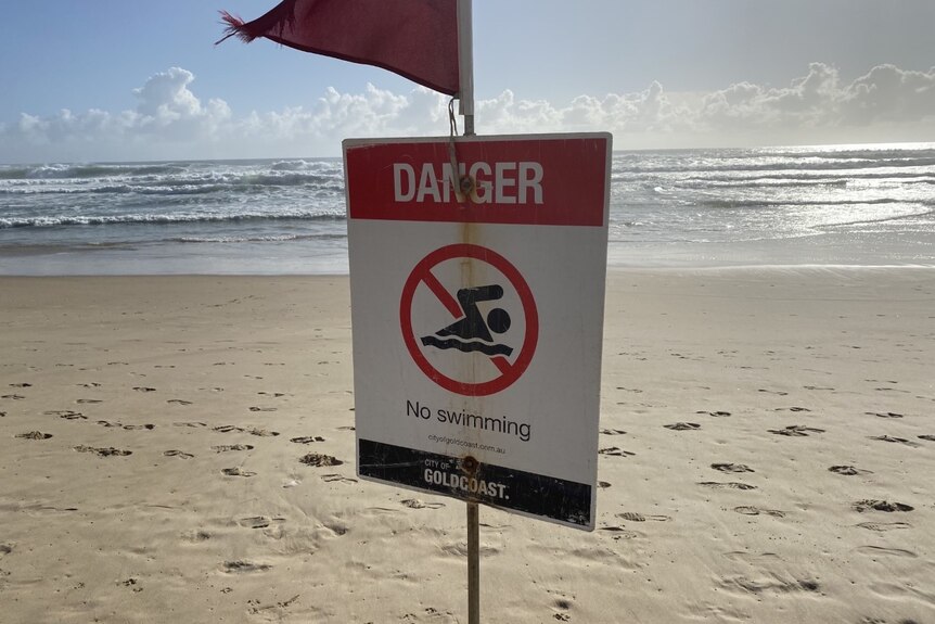 A flag and a sign on the beach reads no swimming.