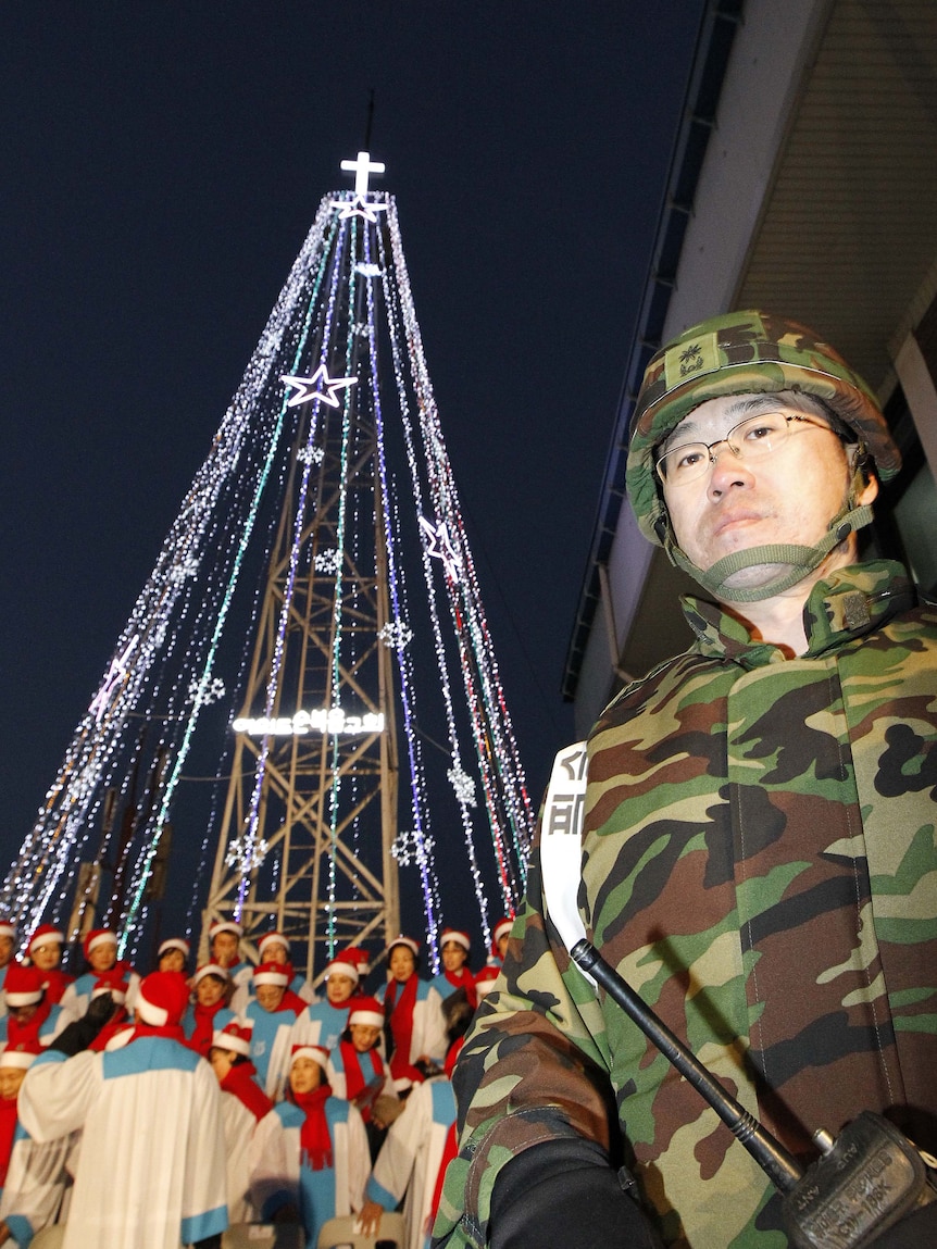 A South Korean military officer stands guard as Christians prepare a lighting ceremony in front of a Christmas tree