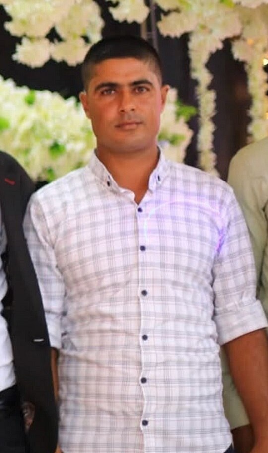 Ahmed Mahmoud Muamar pictured with a dress shirt on and flowers in the background.