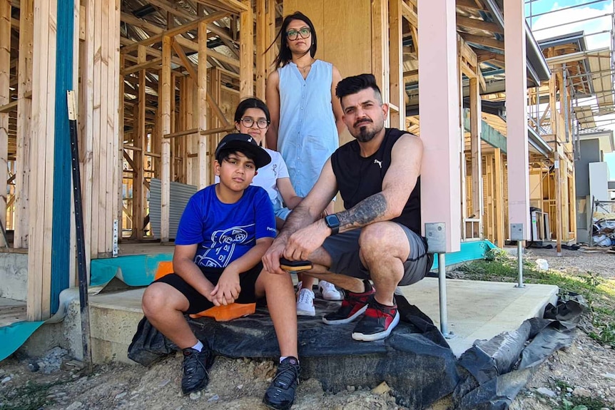 Zainab Akhter stands outside her half built home with her husband and two children