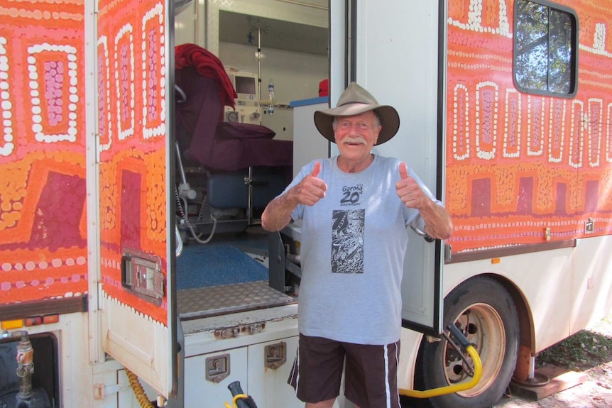 A man wearing a wide brim hat gives a thumbs up standing next to a brightly coloured truck