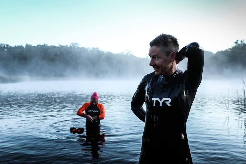 Jessie, with Frog in the background, adjusting her full-length wetsuit.