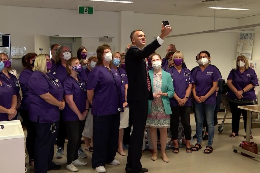 SA Opposition Leader Peter Malinauskas holds up his phone and takes a selfie surrounded by nurses. 