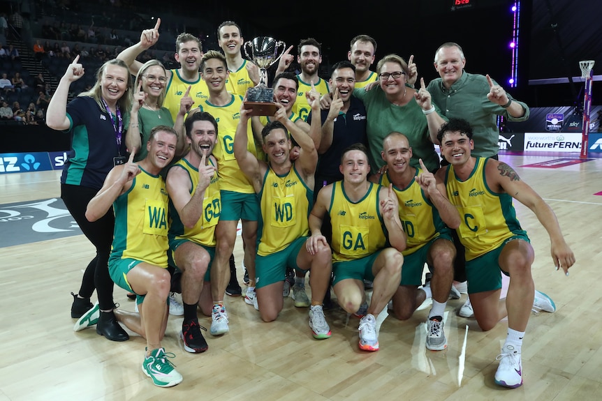 The Aussie men's team wearing green and gold pose together as the captain lefts the trophy overhead