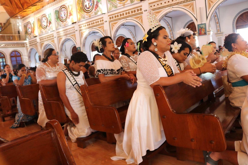 Pews of Samoan women in white wedding-style dresses are pictured kneeling and praying.