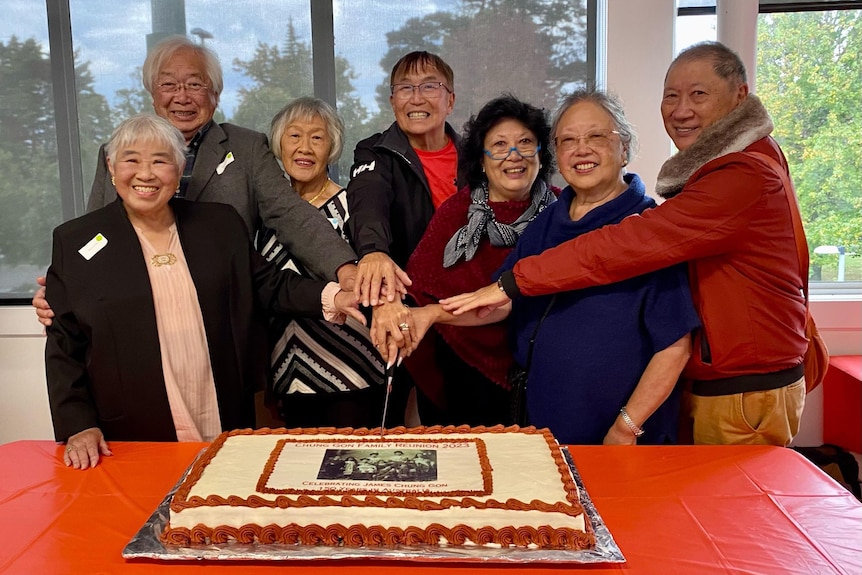 7 older people smile as they cut a cake 