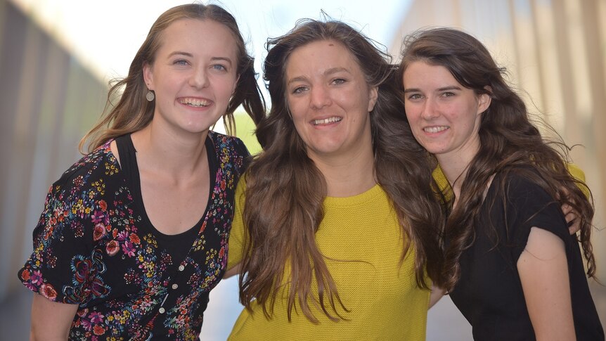 Three woman smile at the camera with a blurred corridor behind them