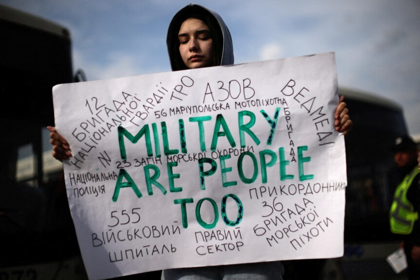A woman holds a sign saying 'military are people too' written on it