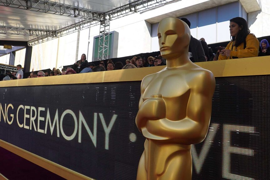 2018 Oscars statue stands in front of crowds gathered in the bleachers on the red carpet.