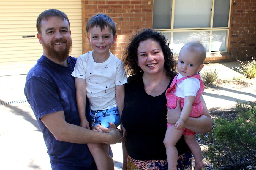 A family smiles at the camera in front of their new home.