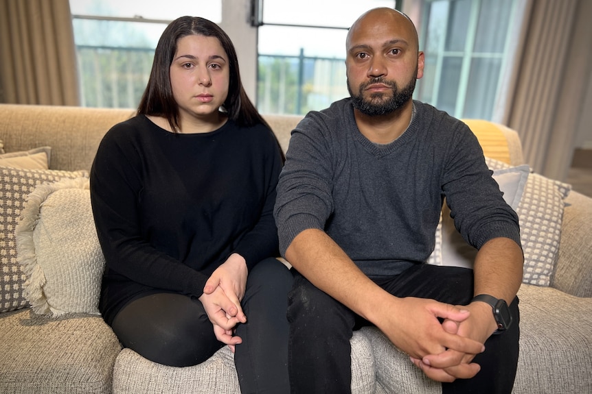 A man and woman wearing black sitting on a light-coloured couch.