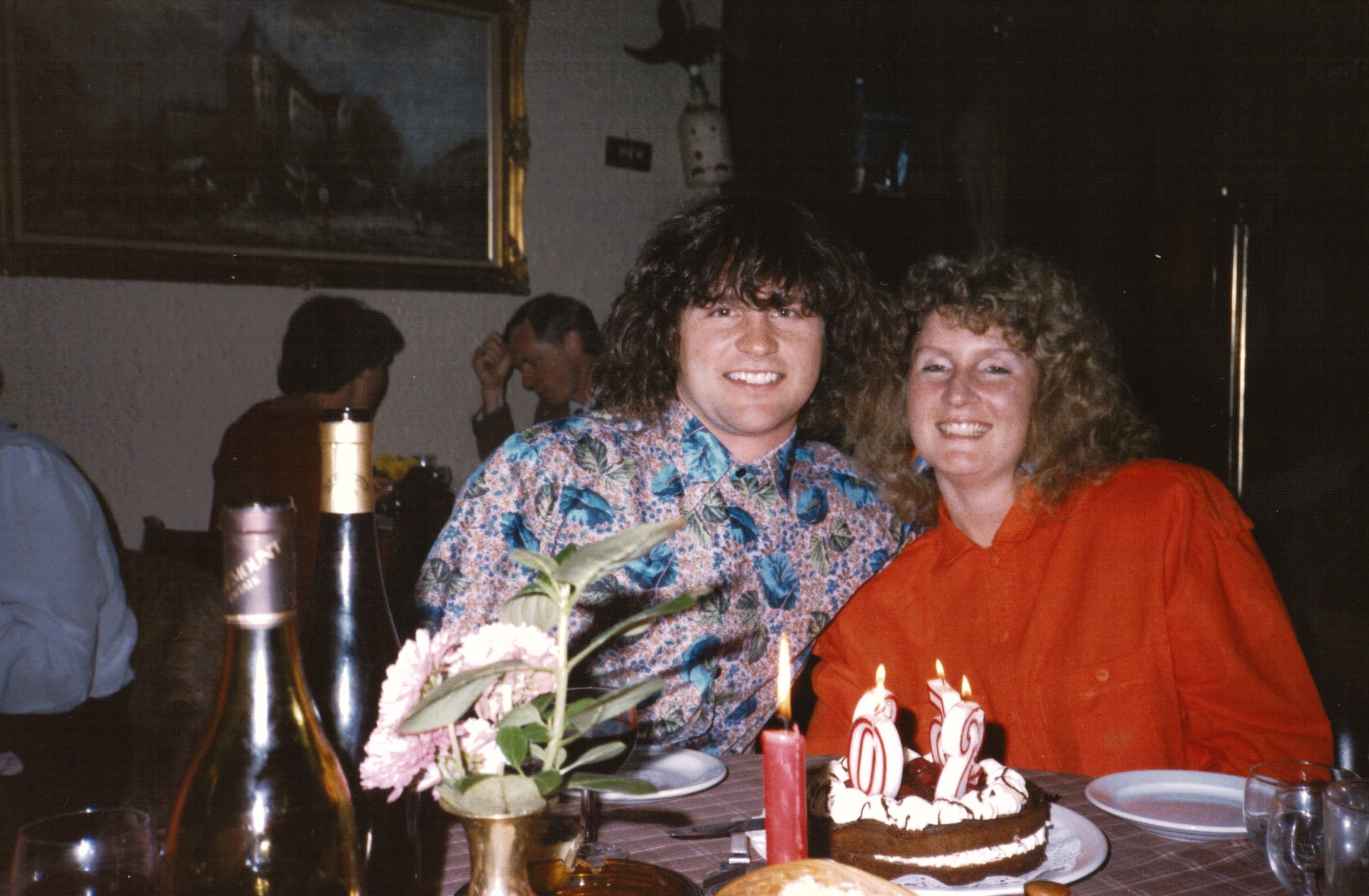 A young man and woman sit together smiling at a table with a birthday cake.