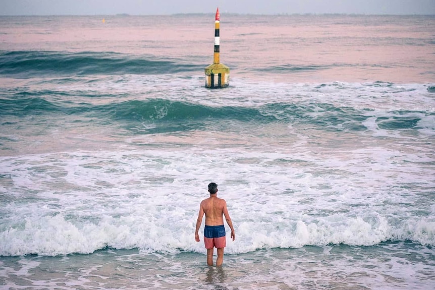 A man enters the water at the beach as the sun rises.