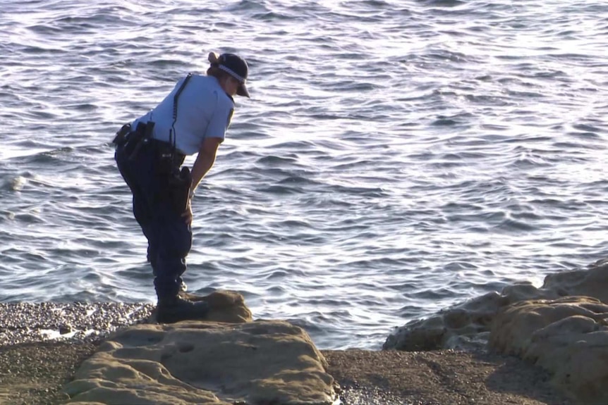 A female police officer stands on a rock, leaning over to look into water