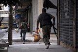 Grip tightens - fighters carrying food supplies run for cover along a street in the Salaheddin district.