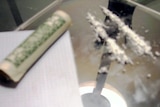 Lines of cocaine and a rolled-up note lie on a glass table.