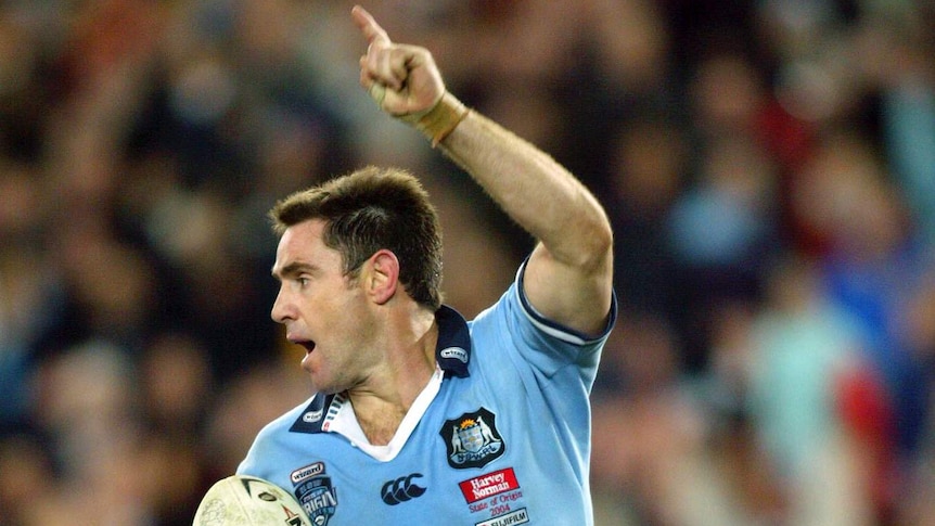Brad Fittler runs with his left armin the air and the ball under his right arm.