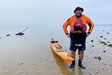 A man wearing high vis stands next to a orange kayak which is floating in the water