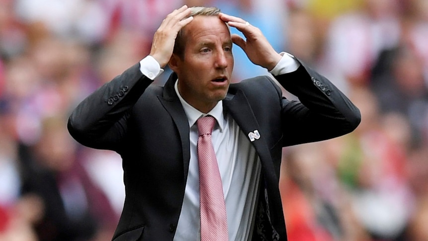 Lee Bowyer holds his hands to his head and looks on in shock wearing a dark suit