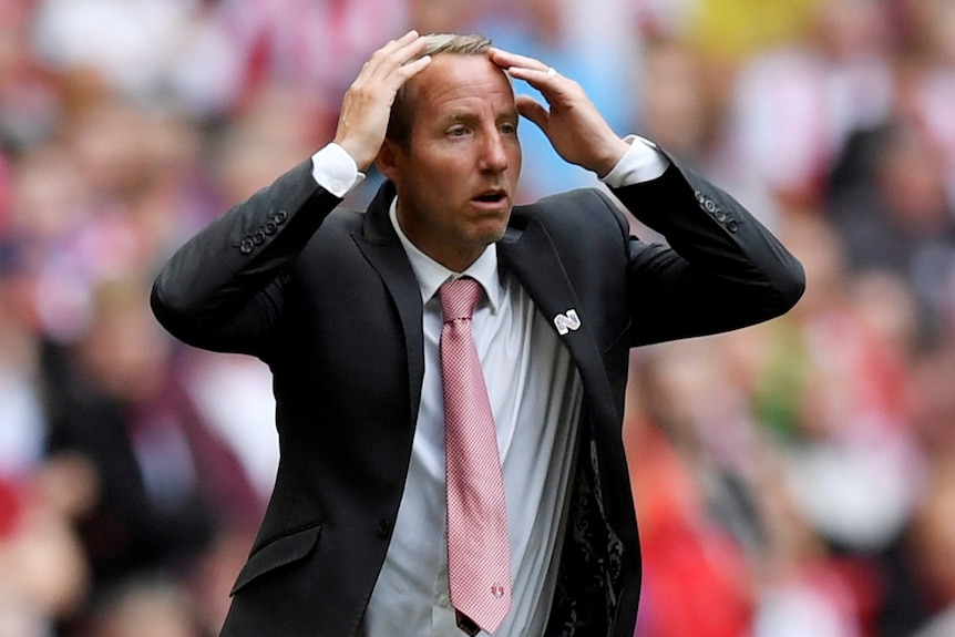 Lee Bowyer holds his hands to his head and looks on in shock wearing a dark suit