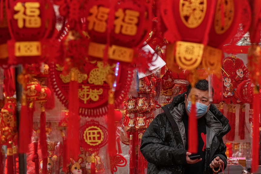 A man wearing a face mask walks among hanging Chinese new year decorations.