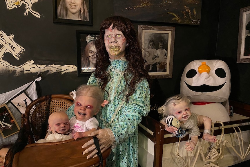 A large ghost doll with scars on her face stands with three evil-looking baby dolls.