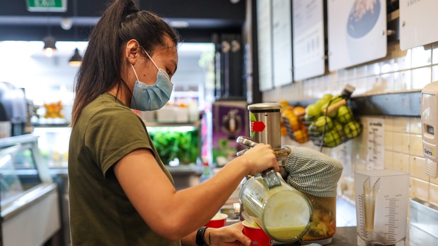 A worker wearing a mask pours a drink into a cup.