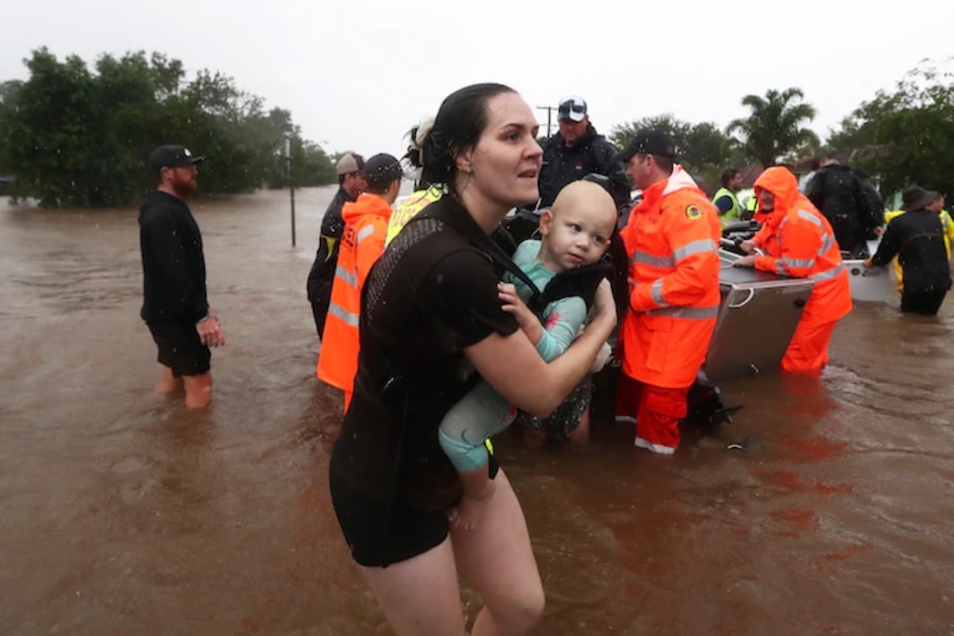 A mother carries her baby after being rescued from floodwaters in Lismore.
