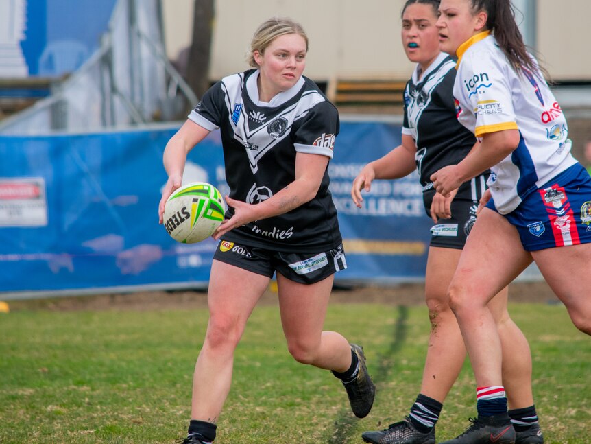A female halfback passing a rugby ball flanked by two other players