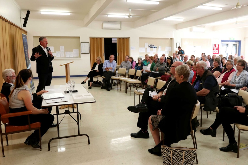 A man addresses a room full of seated people.