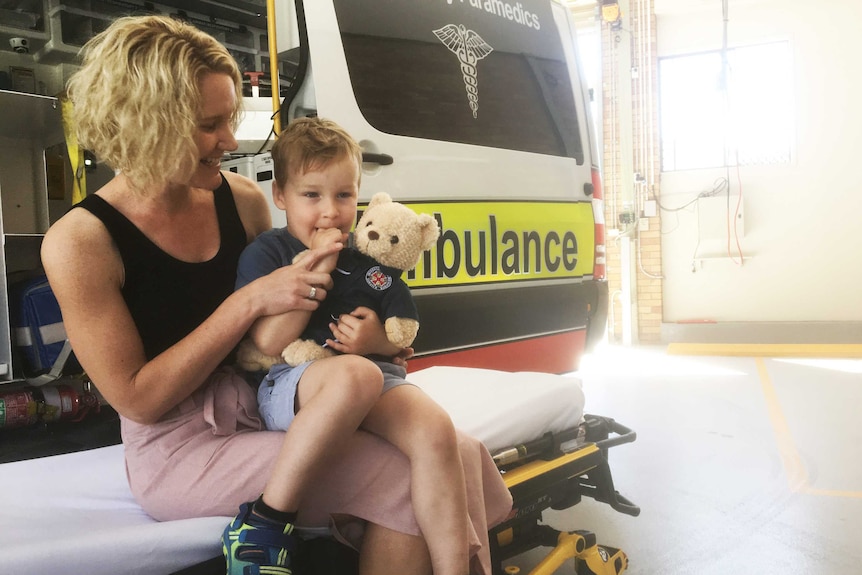 Thomas Skrypinski sitting on an ambulance stretcher with his smiling mother.