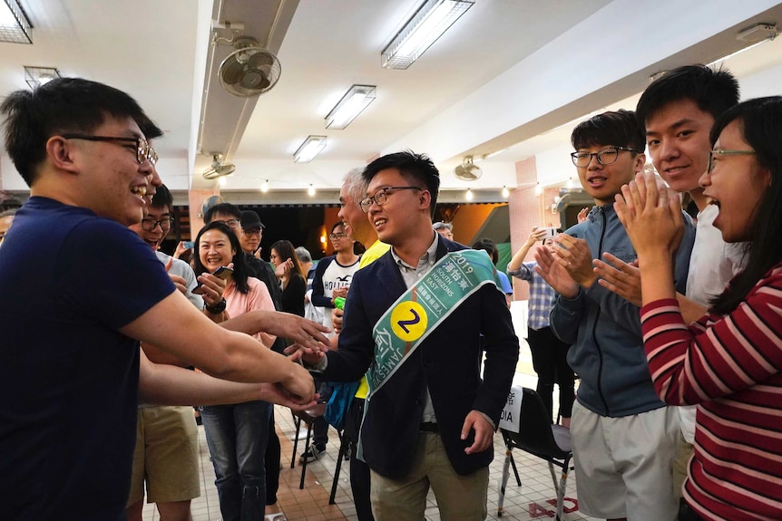 A candidate, wearing a green sash, smiles as he shakes peoples' hands