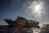 Hundreds of migrants sit on an overcrowded boat in the middle of the ocean.