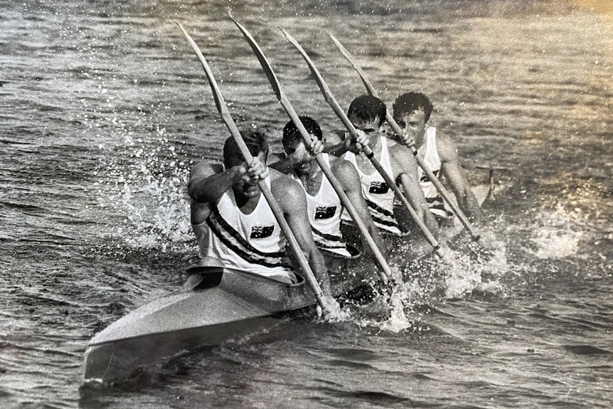 A black and white photo of four men in a kayak training on water.