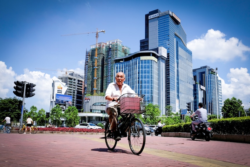 A man on a bicycle cycles past a city skyline, under construction
