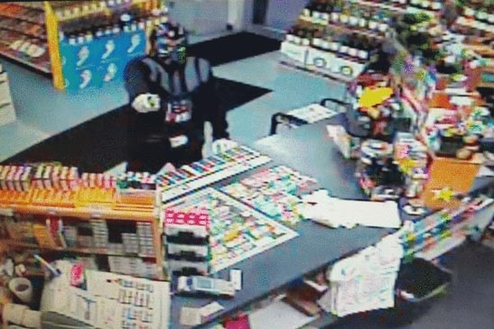 CCTV still of man dressed as Darth Vader pointing gun at store clerk