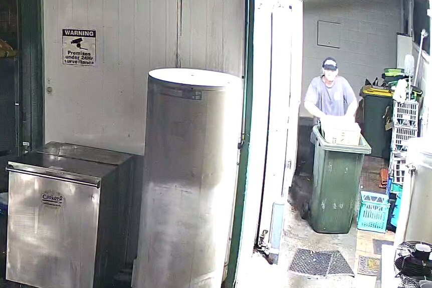 A man wheels a wheelie bin through a butcher shop.