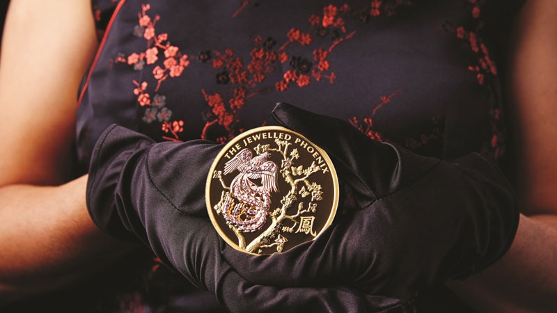 A close up of a lady holding a Jewelled Phoenix coin set with pink diamonds