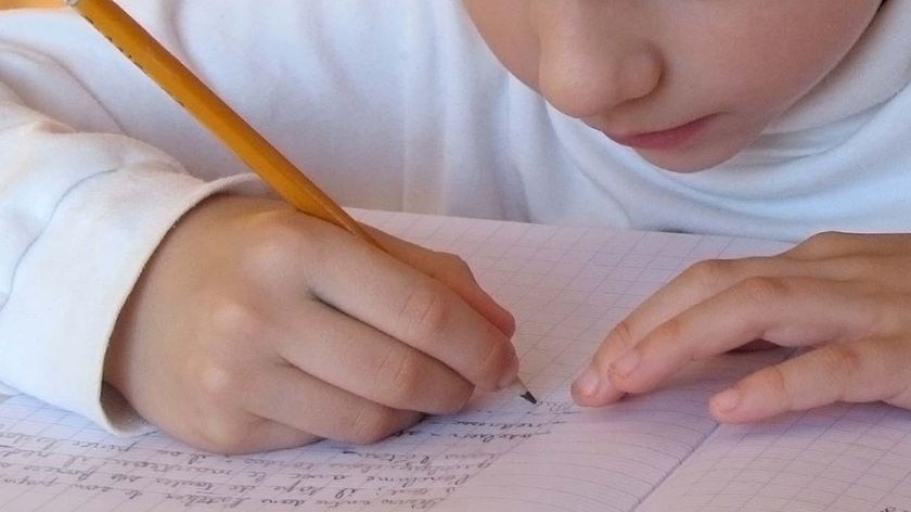 A young child writes in an exercise book in a classroom