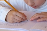 A young child writes in an exercise book in a classroom