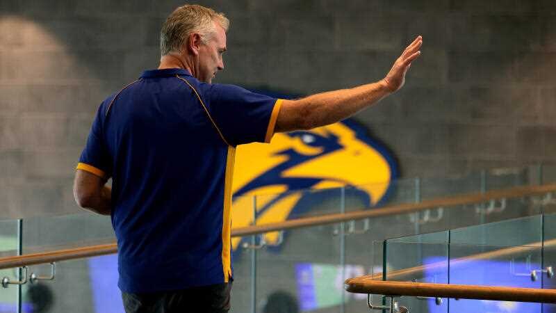 Adam Simpson waving at a media conference.