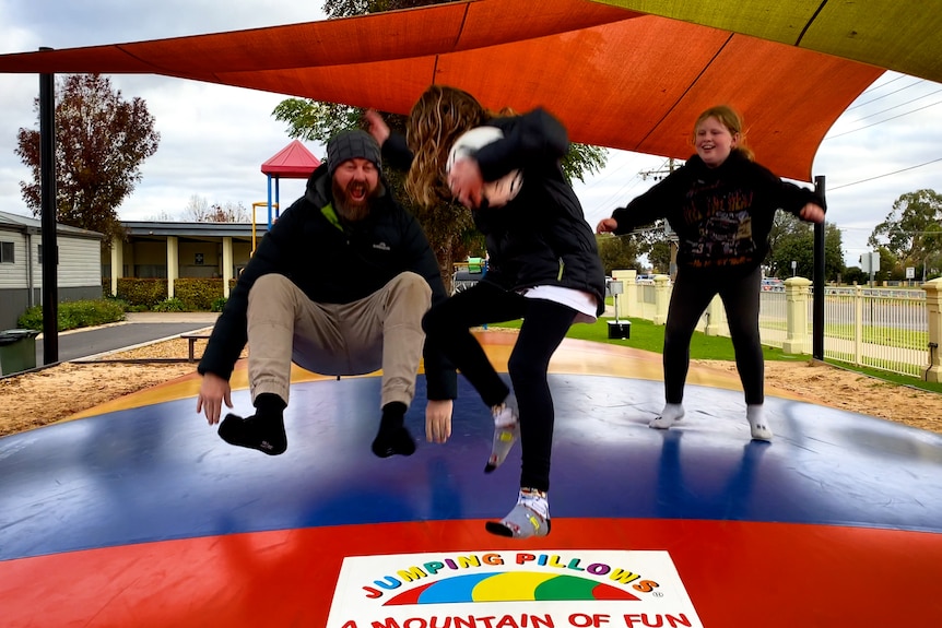 Dad jumping on inflated pillow at caravan park with children