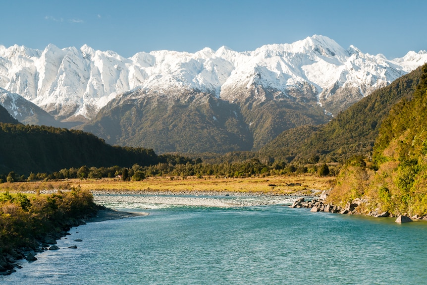 A landscape shot of a bright blue river, green and snow-capped mountains.  