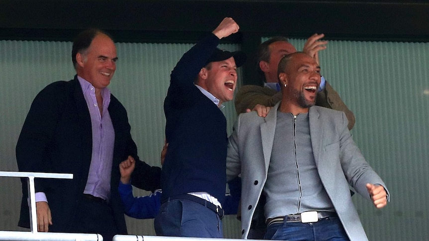 Prince William and another man in the stands celebrate a goal in a soccer match.