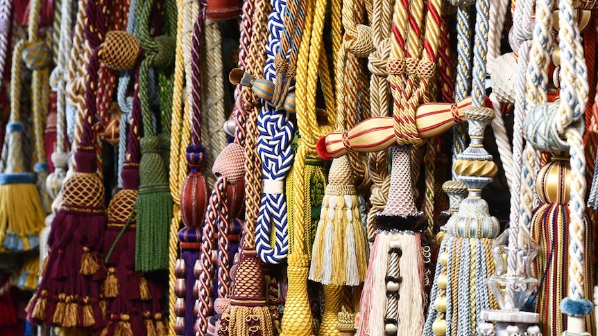 A row of passementerie hang from a wall, showing off an array of colours and textures. 