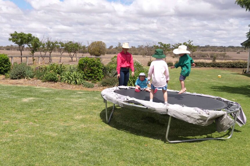 Three children bounce on a trampoline in broad brimmed hats