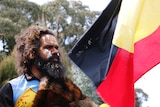 Clinton Pryor holds and looks at an Aboriginal flag.